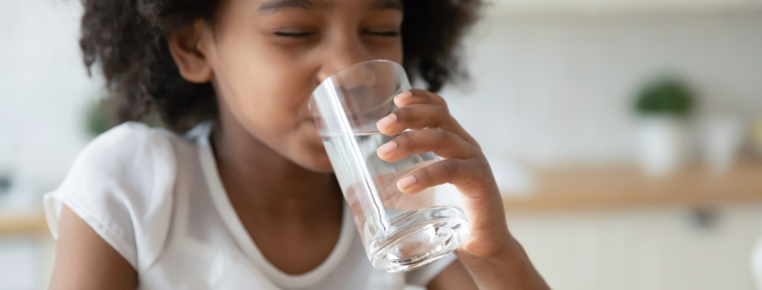Une jeune fille buvant dans un verre d'eau.