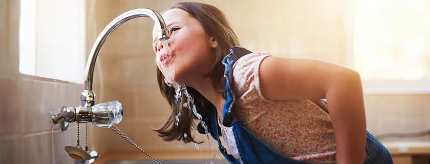 Une jeune fille buvant directement au robinet de la cuisine.