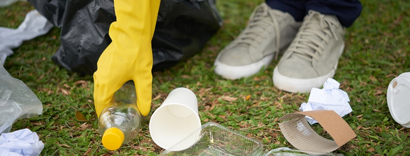 Une personne portant des gants jaunes ramasse des déchets dans l'herbe.